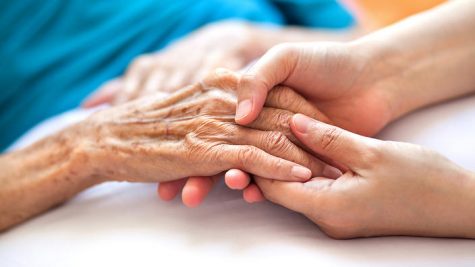 Woman holding senior woman's hand on bed